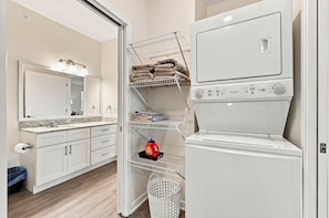 A laundry room with a stacked washer and dryer, shelves for towels and laundry, a sink, and a mirror. - MALACHI 353 - 1 King bed - Pickleball (Noblesville)