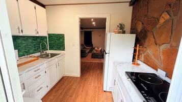 Une cuisine de taille réduite avec des meubles blancs, un pare-feu vert, un plancher en bois et un mur d’accent en pierre.