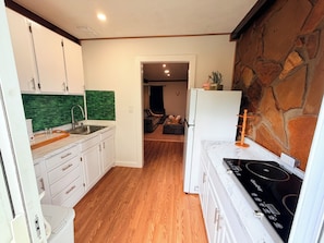 Une cuisine de taille réduite avec des meubles blancs, un pare-feu vert, un plancher en bois et un mur d’accent en pierre.
