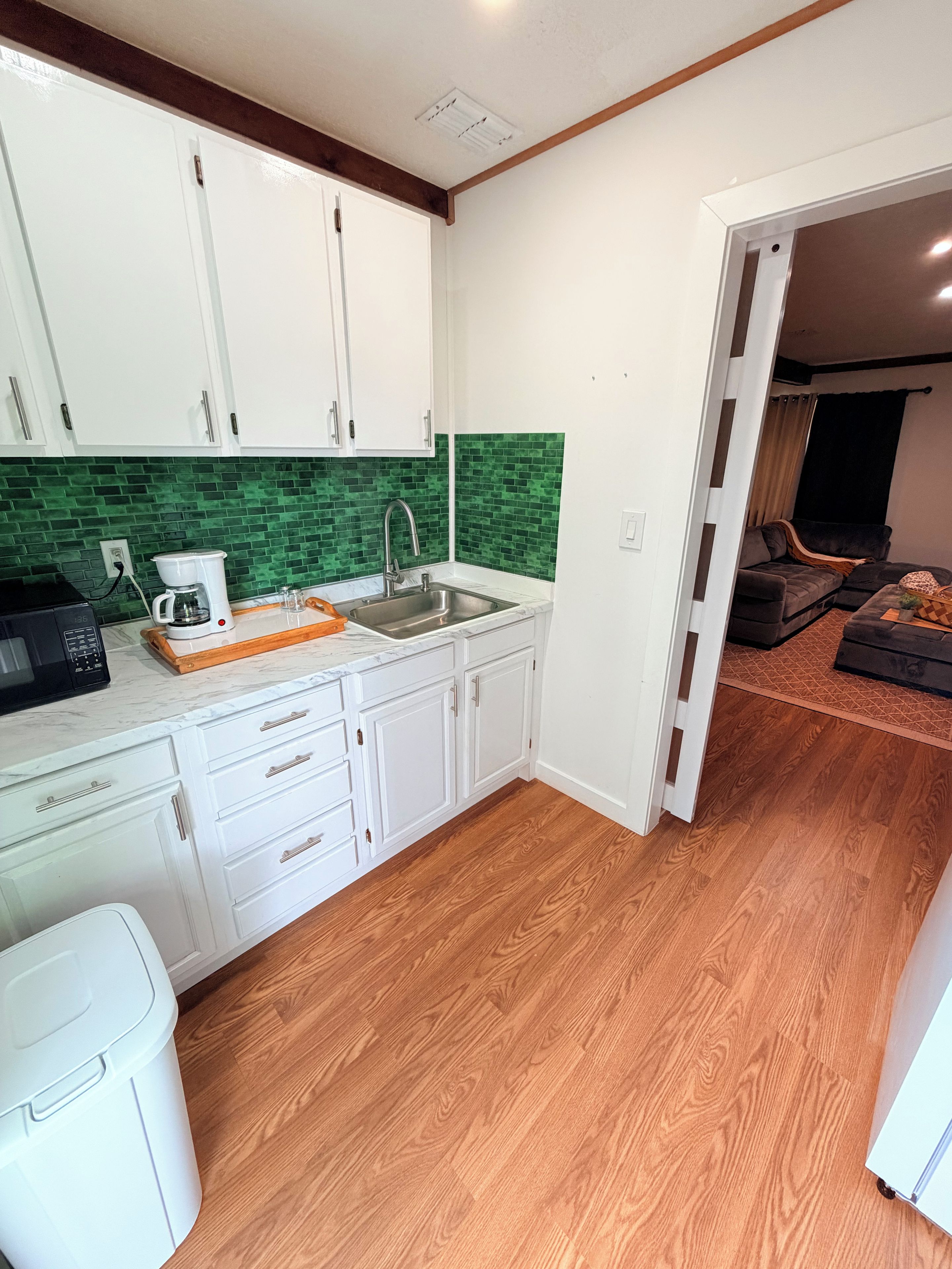 A compact kitchen with white cabinets, a green backsplash, and a wooden floor.