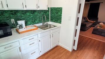 A compact kitchen with white cabinets, a green backsplash, and a wooden floor.