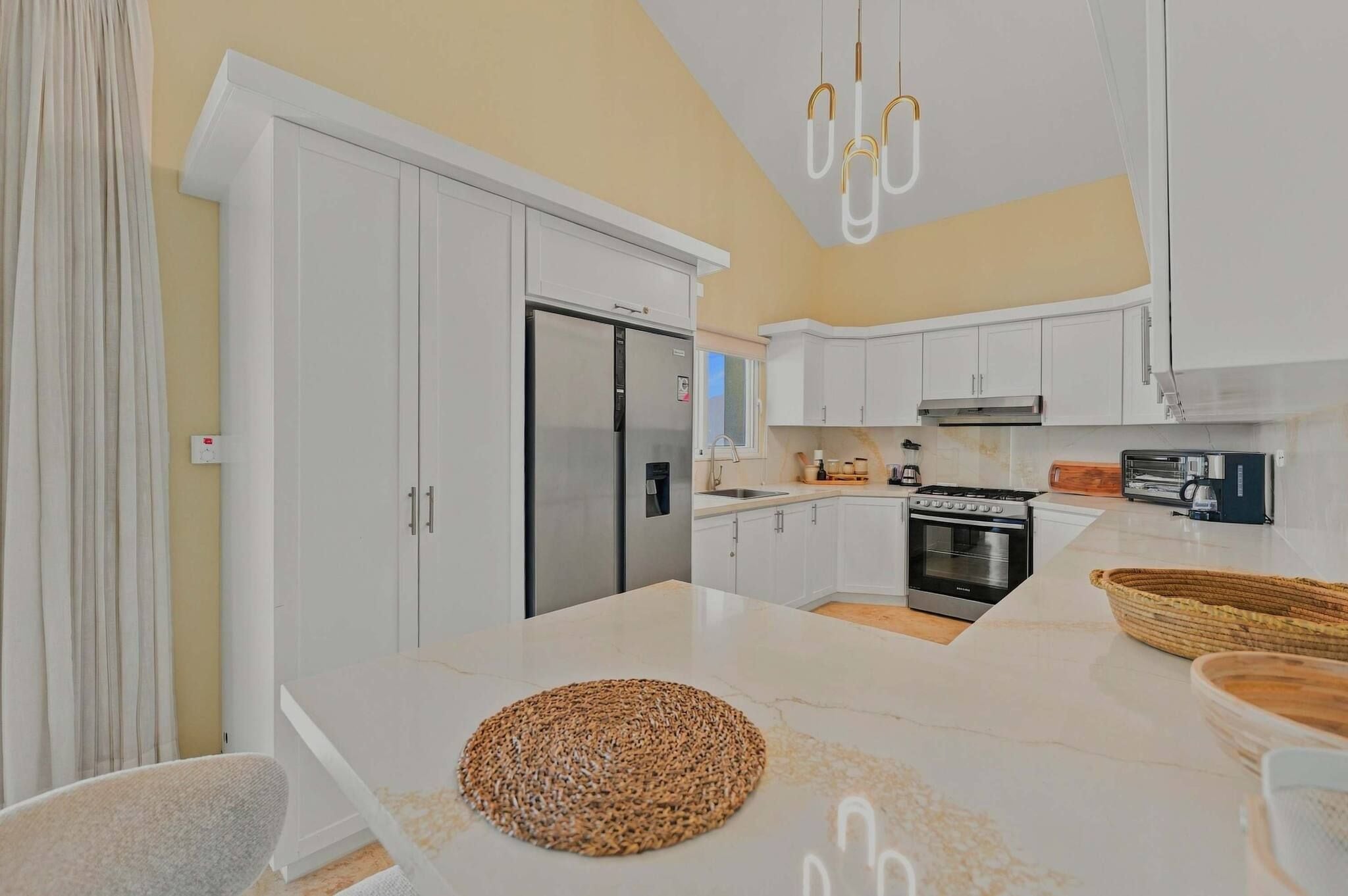 A modern kitchen with white cabinetry, a stainless steel refrigerator, a built-in oven, and a coffee machine.
