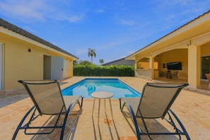 A swimming pool with two lounge chairs facing it, surrounded by a covered patio area with a table and chairs. - 4BR Caribbean Villa in Hispaniola (Sosúa)