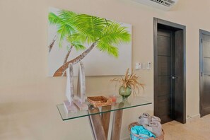 A hallway with a glass-top table displaying a vase, a candle, and a woven basket. A painting of a palm tree is on the wall. - 4BR Caribbean Villa in Hispaniola (Sosúa)