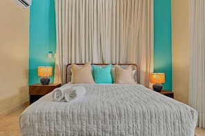 A hotel room with a bed, two bedside lamps, a window with curtains, and a wall-mounted air conditioning unit. - 4BR Caribbean Villa in Hispaniola (Sosúa)