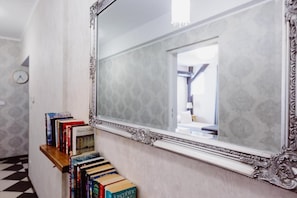 A hallway with a large mirror, a clock, and a row of books on a shelf. - Kings City Zyblikiewicza 5  (Kraków)