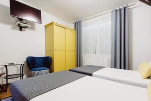Une chambre d’hôtel avec deux lits, un téléviseur fixé au mur, une armoire jaune et une chaise.