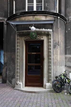 Une entrée d’immeuble avec une porte marron, une enseigne verte au-dessus, et un vélo garé sur le côté.