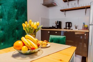A kitchen with a dining table set with fruits, a bowl of bananas, and a vase of tulips. - Kings City Zyblikiewicza 5  (Kraków)