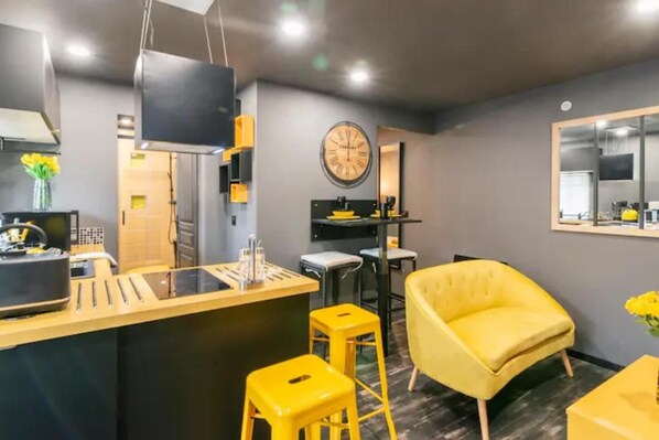 A modern kitchen with a central island, bar stools, a yellow chair, and a large wall clock. - Vrbo Property (Angoulême)