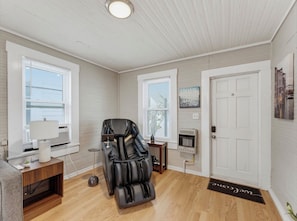 Une pièce équipée d’un fauteuil de massage, d’une petite table avec une lampe, d’un radiateur et d’une porte avec un paillasson.
