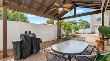 Un patio couvert avec un barbecue, une table et des chaises.
