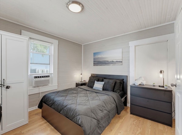 Une chambre à coucher avec un lit, des tables de chevet, une commode, une fenêtre et un tableau au mur.