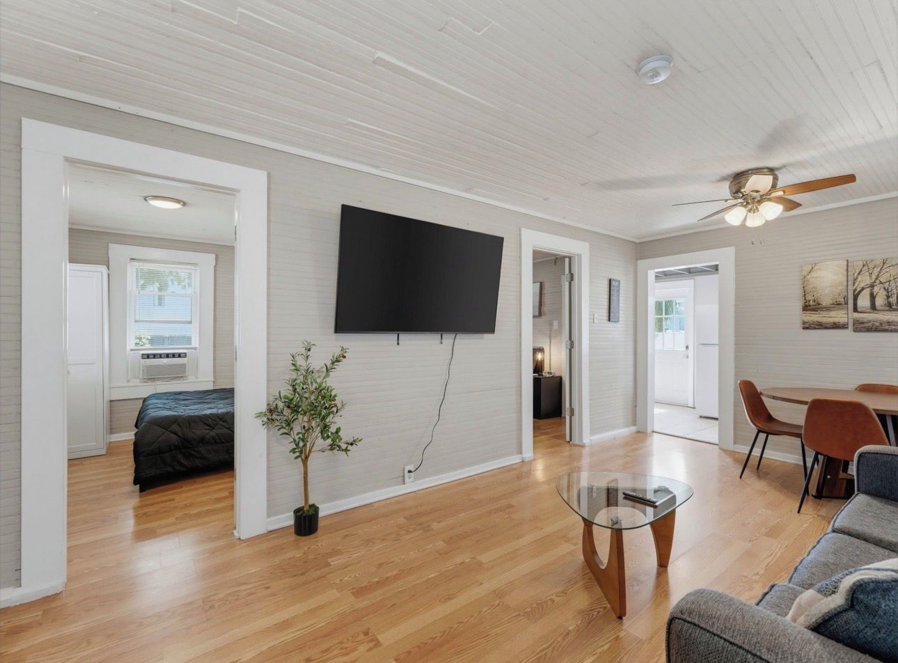 A spacious living area with a flat-screen TV mounted on the wall, a glass coffee table, a sofa, and a dining table with chairs.