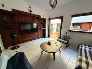 A living room with a television, a coffee table, a sofa, and a window with a view. - Pousada Villavera (Caraguatatuba)