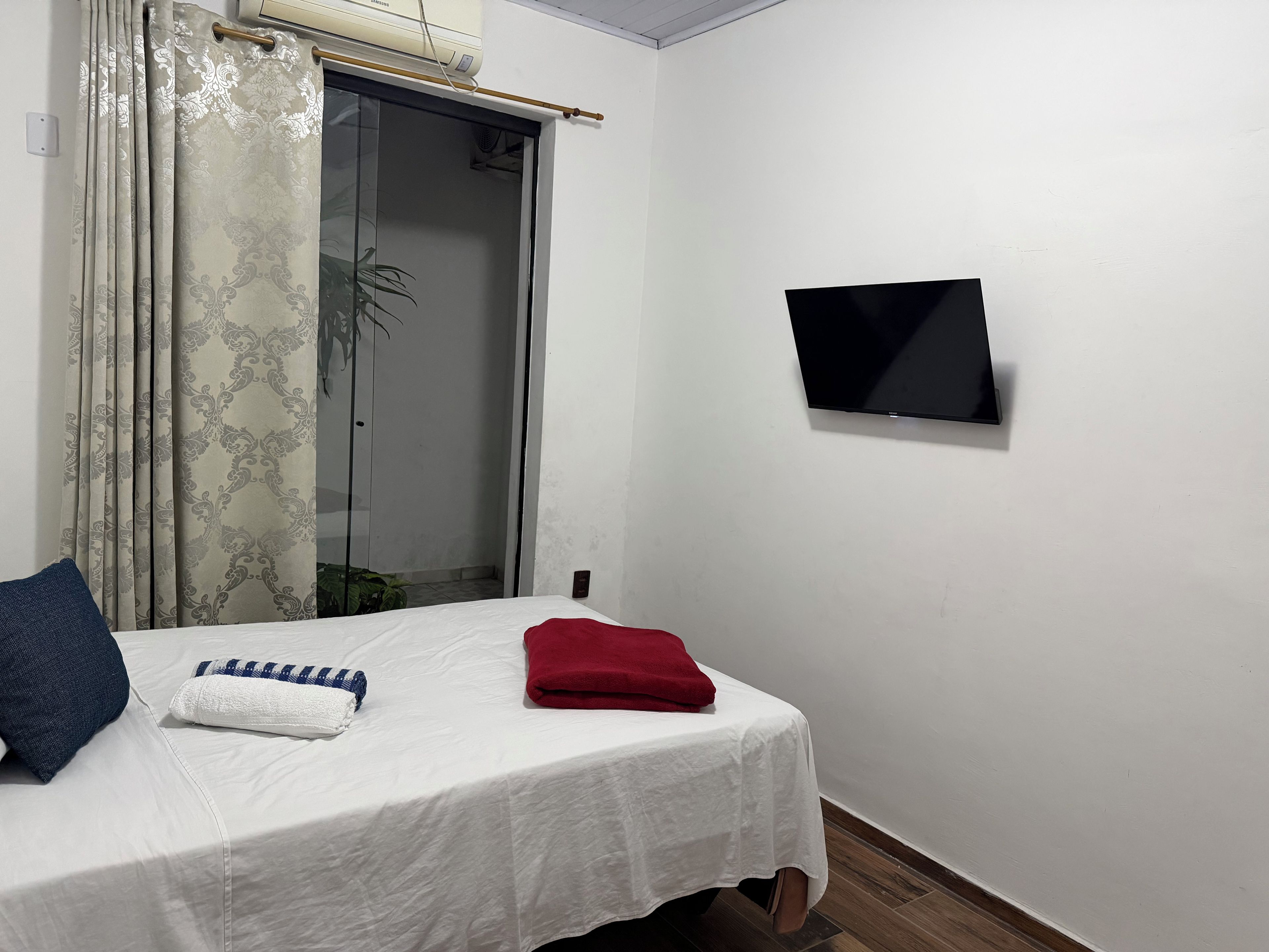 Una habitación con cama, televisor montado en la pared y puerta corredera de vidrio.