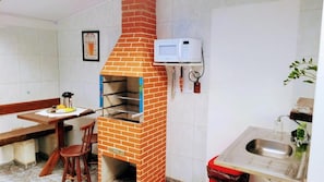 A kitchen with a brick oven, a microwave, a sink, and a dining area with chairs. - Pousada Villavera (Caraguatatuba)