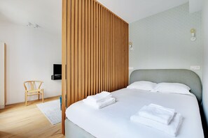 A modern hotel room with a large bed, a wooden partition, a small chair, and a flat-screen TV. - Amazing Studio 2P- Arc de Triomphe-champs Elyse (Paris)