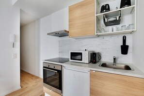 A modern kitchen with a built-in oven, microwave, and dishwasher, wooden cabinets, and a marble backsplash. - Amazing Studio 2P- Arc de Triomphe-champs Elyse (Paris)