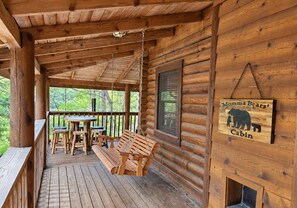 A wooden cabin with a porch, a table, benches, and a hanging sign. - Gatlinburg Log Cabin | Spa - Games - Arts District (Gatlinburg)