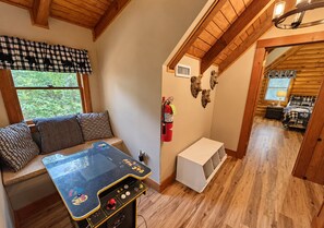 Ein gemütliches Blockhaus-Interieur mit einem Spieltisch, einer Bank mit Kissen, einem Kamin und einem Bett mit karierter Decke.