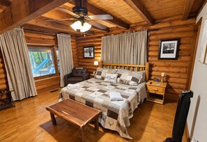 A log cabin bedroom with a bed, a chair, a table, and a ceiling fan. - Gatlinburg Log Cabin | Spa - Games - Arts District (Gatlinburg)