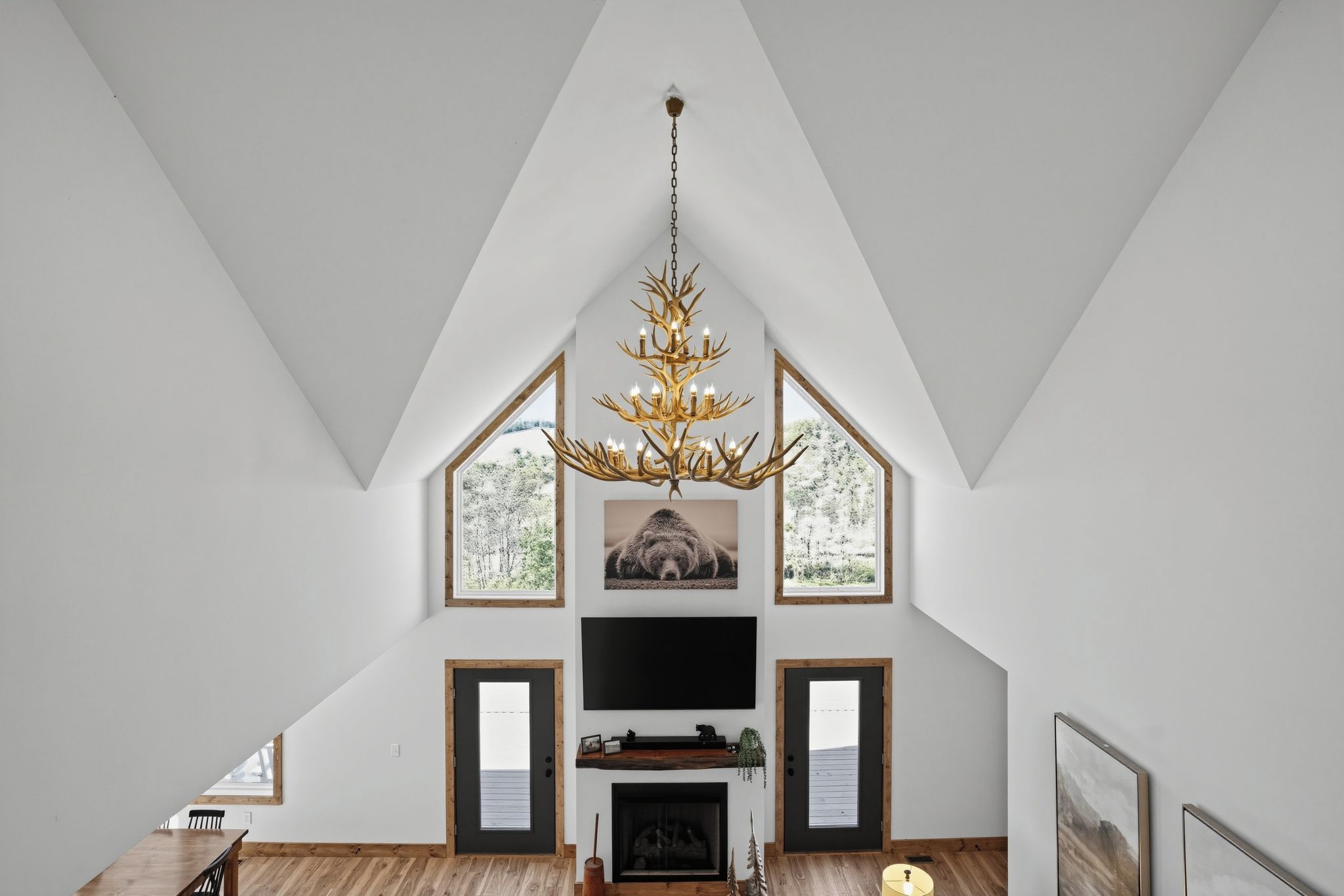 Amplia sala de estar con techo alto, chimenea, televisor y un ventanal con vistas a árboles.