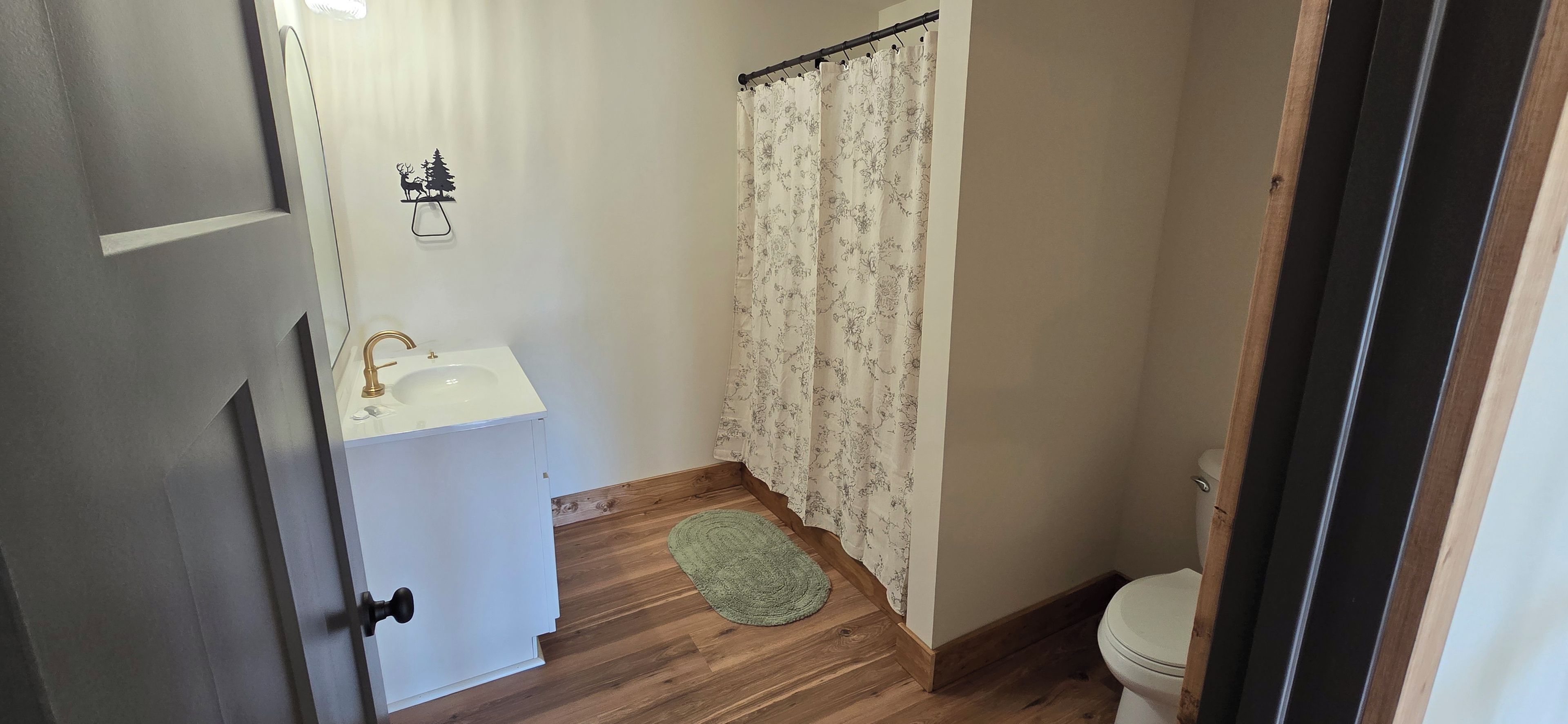 A bathroom with a white sink, a shower curtain, a toilet, and a wooden floor.