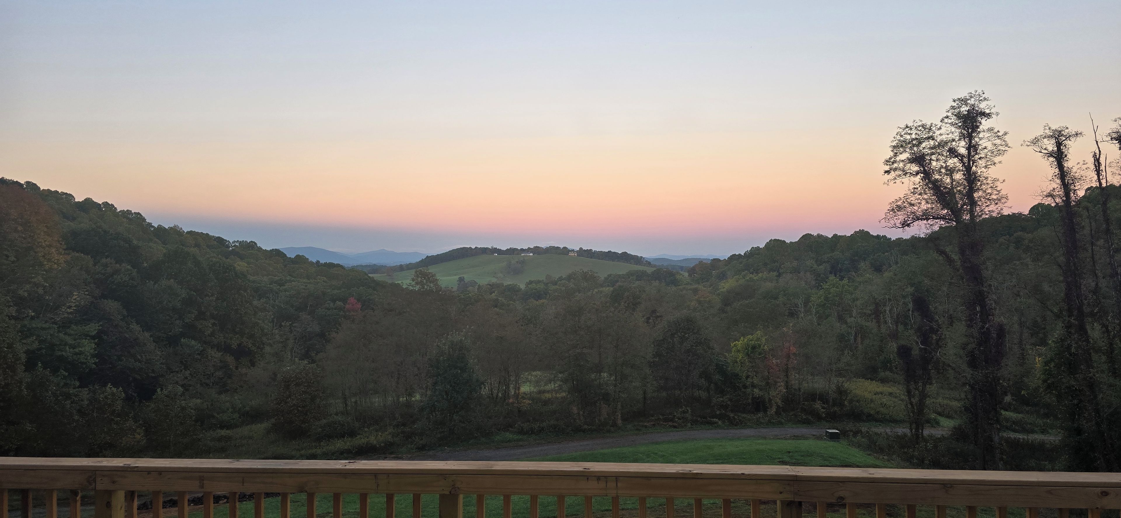 A view from a wooden deck overlooking a forested valley with distant hills.