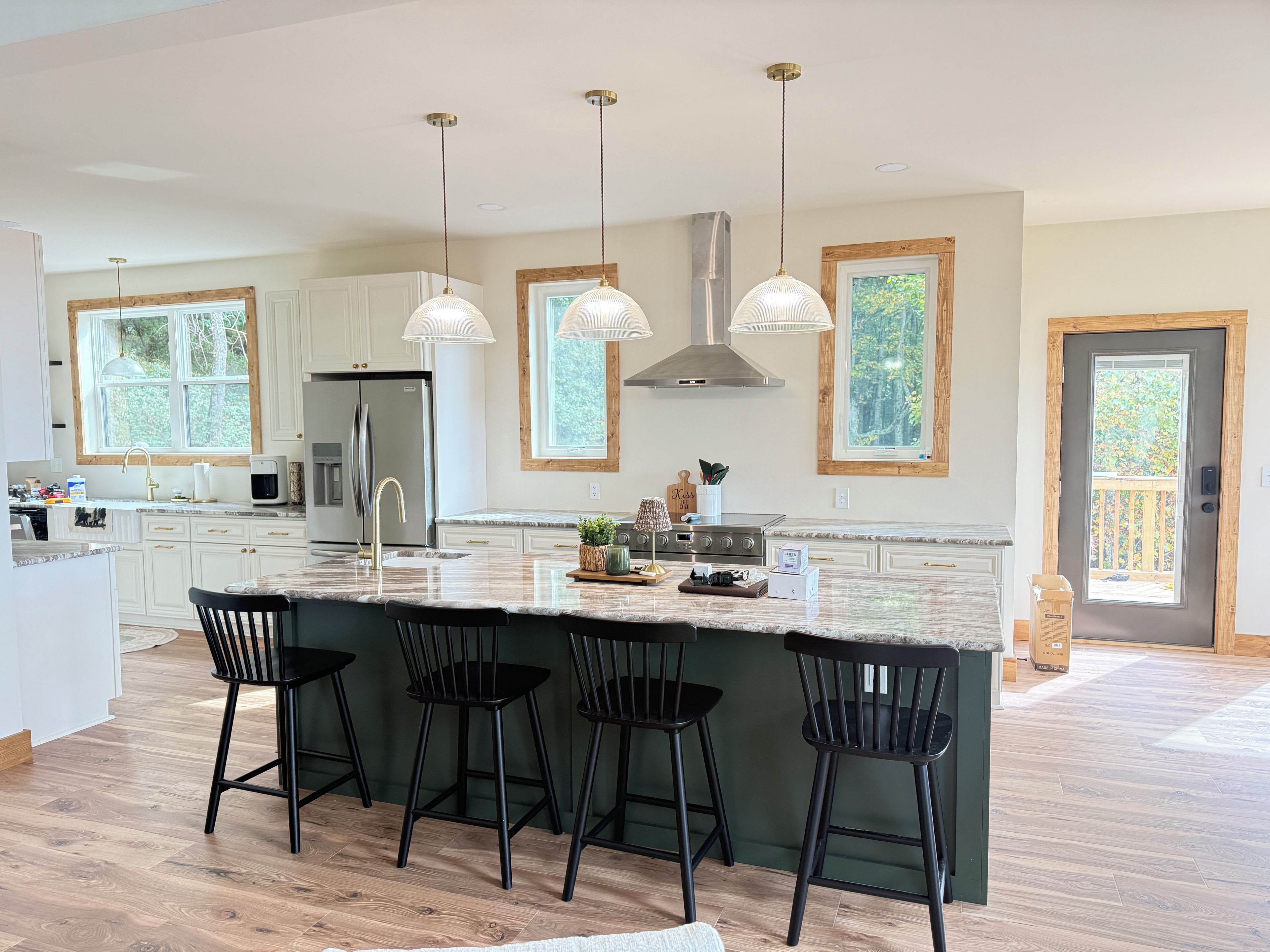 A modern kitchen with a large island, pendant lights, and a view of the outdoors.