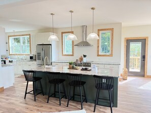 A modern kitchen with a large island, pendant lights, and a view of the outdoors.