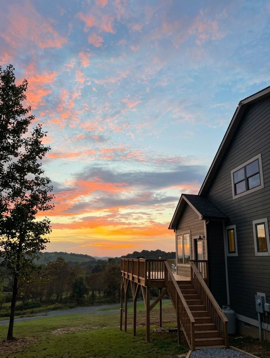 A residential property with a wooden deck, a staircase leading to a covered area, and a view of the landscape.