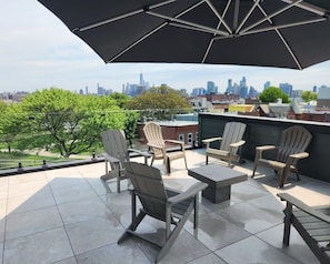 A rooftop terrace with outdoor seating, a large umbrella, and a city skyline view. - NYC Skyline Rooftop · 3BR Row House · Sleeps 9 (Jersey city)