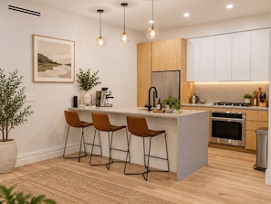 A modern kitchen with a central island, bar stools, a refrigerator, an oven, and a coffee machine. - NYC Skyline Rooftop · 3BR Row House · Sleeps 9 (Jersey city)