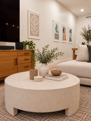 A modern living room with a round coffee table, a sofa, a wooden cabinet, and wall art. - NYC Skyline Rooftop · 3BR Row House · Sleeps 9 (Jersey city)