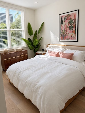 A bedroom with a large bed, a nightstand, a dresser, and a window with blinds. - NYC Skyline Rooftop · 3BR Row House · Sleeps 9 (Jersey city)