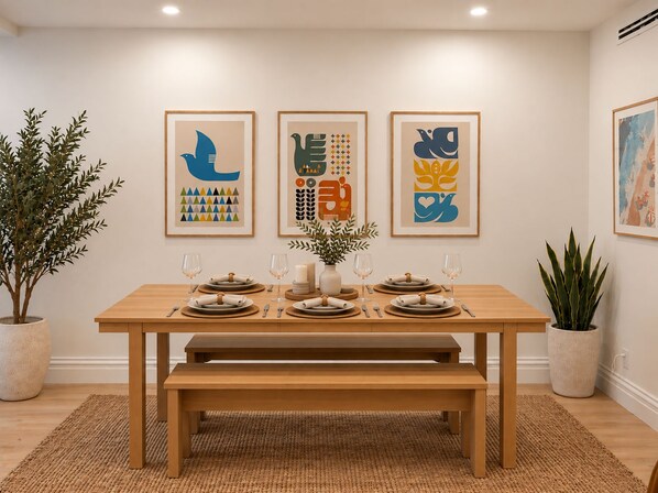 A dining area with a wooden table set for four, framed artwork on the wall, and potted plants. - NYC Skyline Rooftop · 3BR Row House · Sleeps 9 (Jersey city)