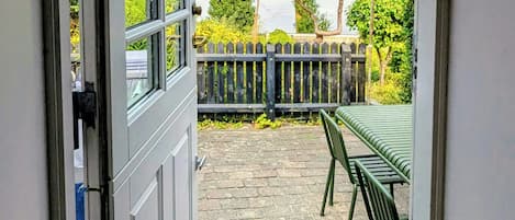 An open door leading to a patio with a table and chairs, a wooden fence, and a view of the sea.