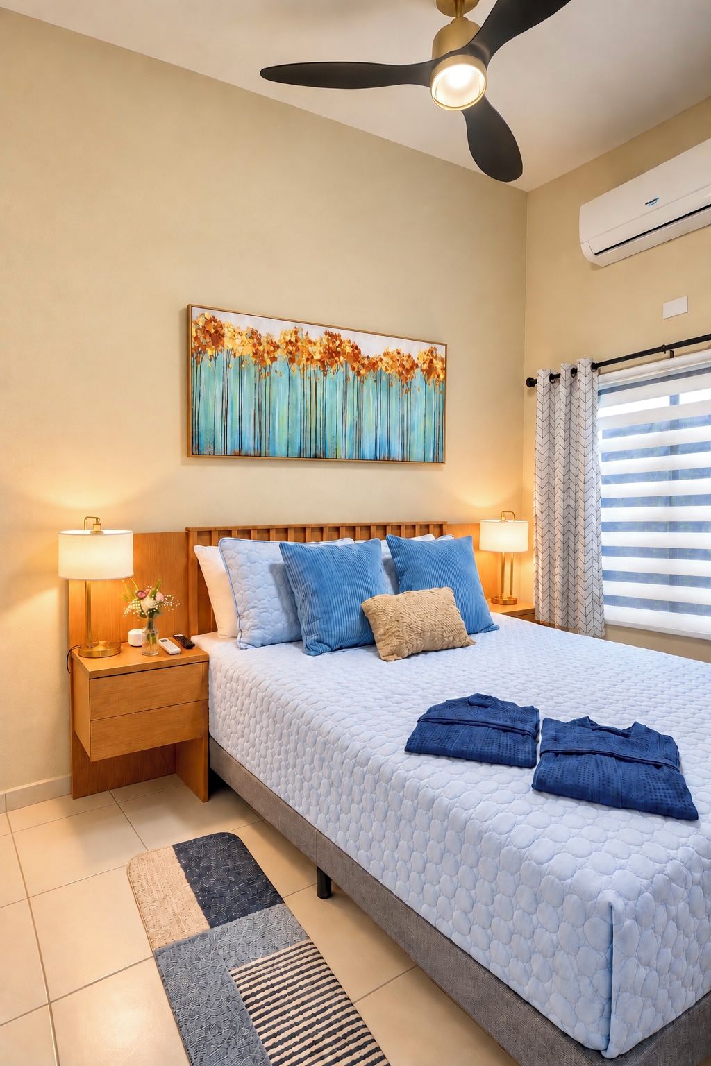 A bedroom with a bed, nightstands, a ceiling fan, an air conditioning unit, a window with curtains, and a wall-mounted painting.