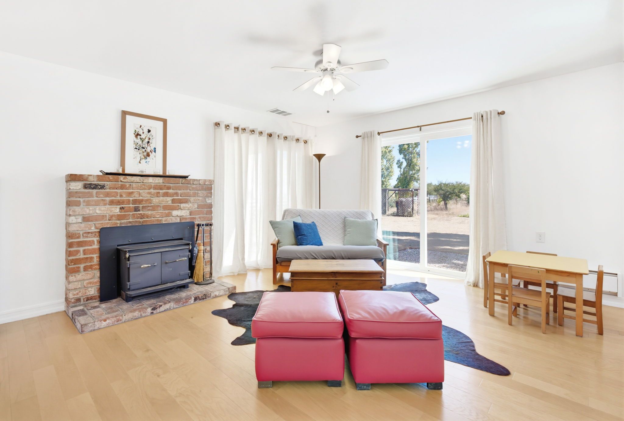 A living room with a fireplace, a sofa, a table, and a view through a sliding glass door.
