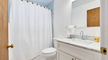 A bathroom with a white toilet, a shower curtain, a sink with a marble countertop, and a mirror above the sink.