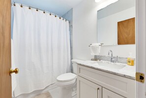 A bathroom with a white toilet, a shower curtain, a sink with a marble countertop, and a mirror above the sink.