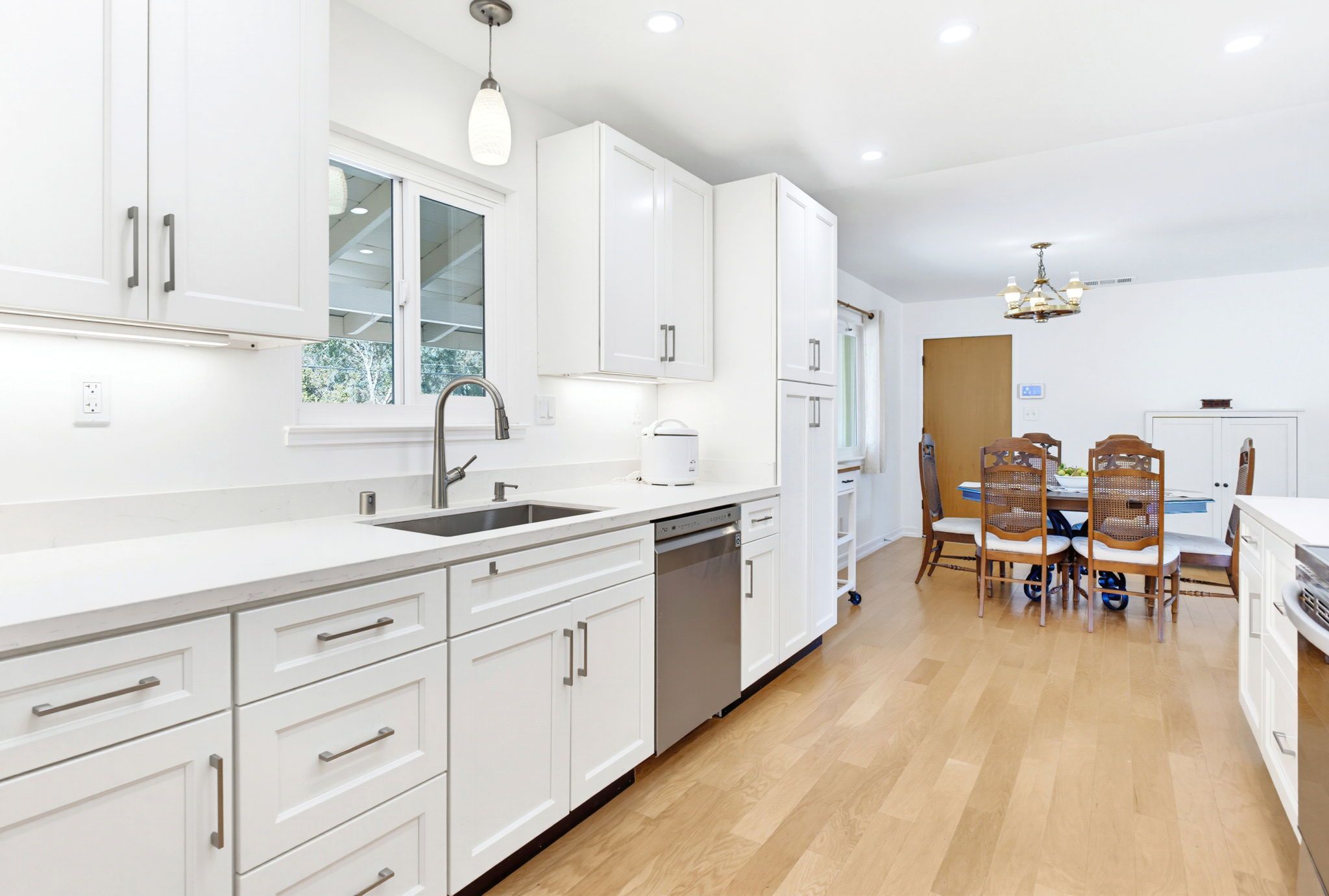 A modern kitchen with white cabinetry, a built-in dishwasher, and a dining area with a wooden table and chairs.