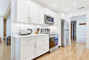 A modern kitchen with white cabinetry, stainless steel appliances, and a wooden floor.