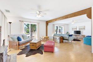 A spacious living area with a sofa, ottoman, wooden chest, and a television.