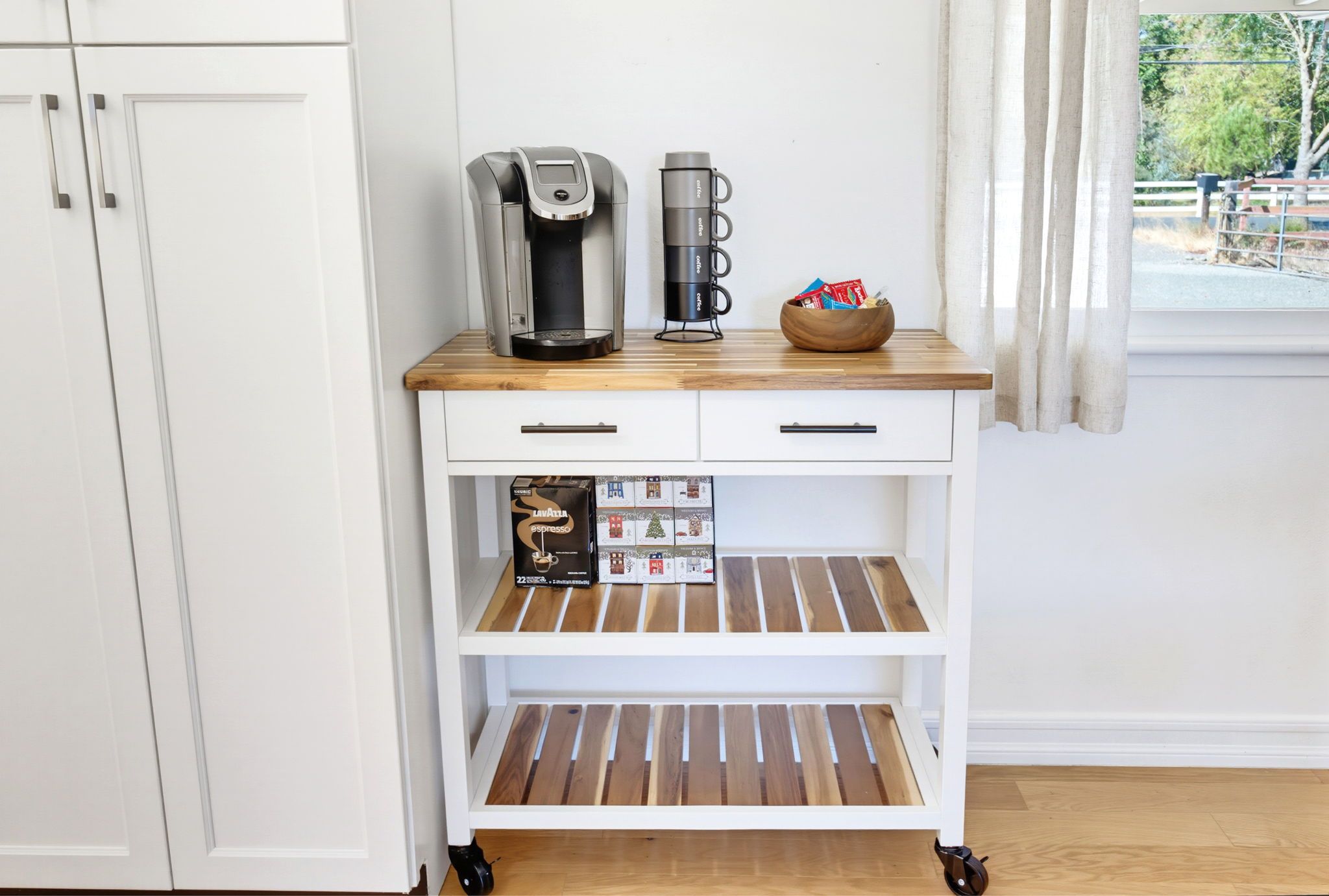 A kitchen counter with a coffee maker, a thermos, and a bowl of snacks. Below are coffee pods and a box of coffee creamer.