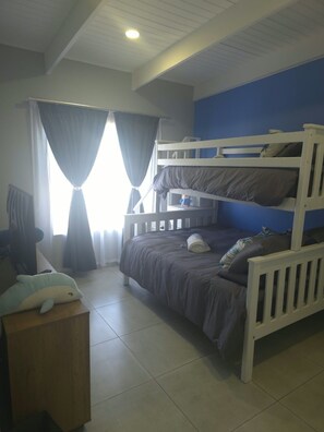 Habitación con literas, una ventana, cortinas y un peluche sobre una mesita de noche de madera.