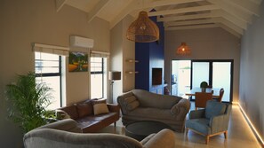 Uma sala de estar ampla com um sofá grande, uma poltrona menor e um espaço de refeições com mesa e cadeiras.