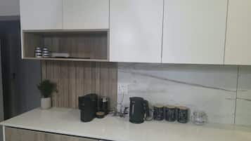 A modern kitchen with white cabinets, a marble backsplash, and a countertop with coffee-making equipment and mugs.