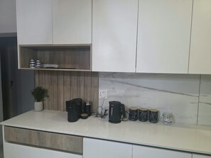 Una cocina moderna con armarios blancos, un salpicadero de mármol y una encimera con equipo para preparar café y tazas.